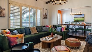 Un salon avec un canapé vert, une table basse en bois et un coin repas comprenant une table et des chaises en bois.
