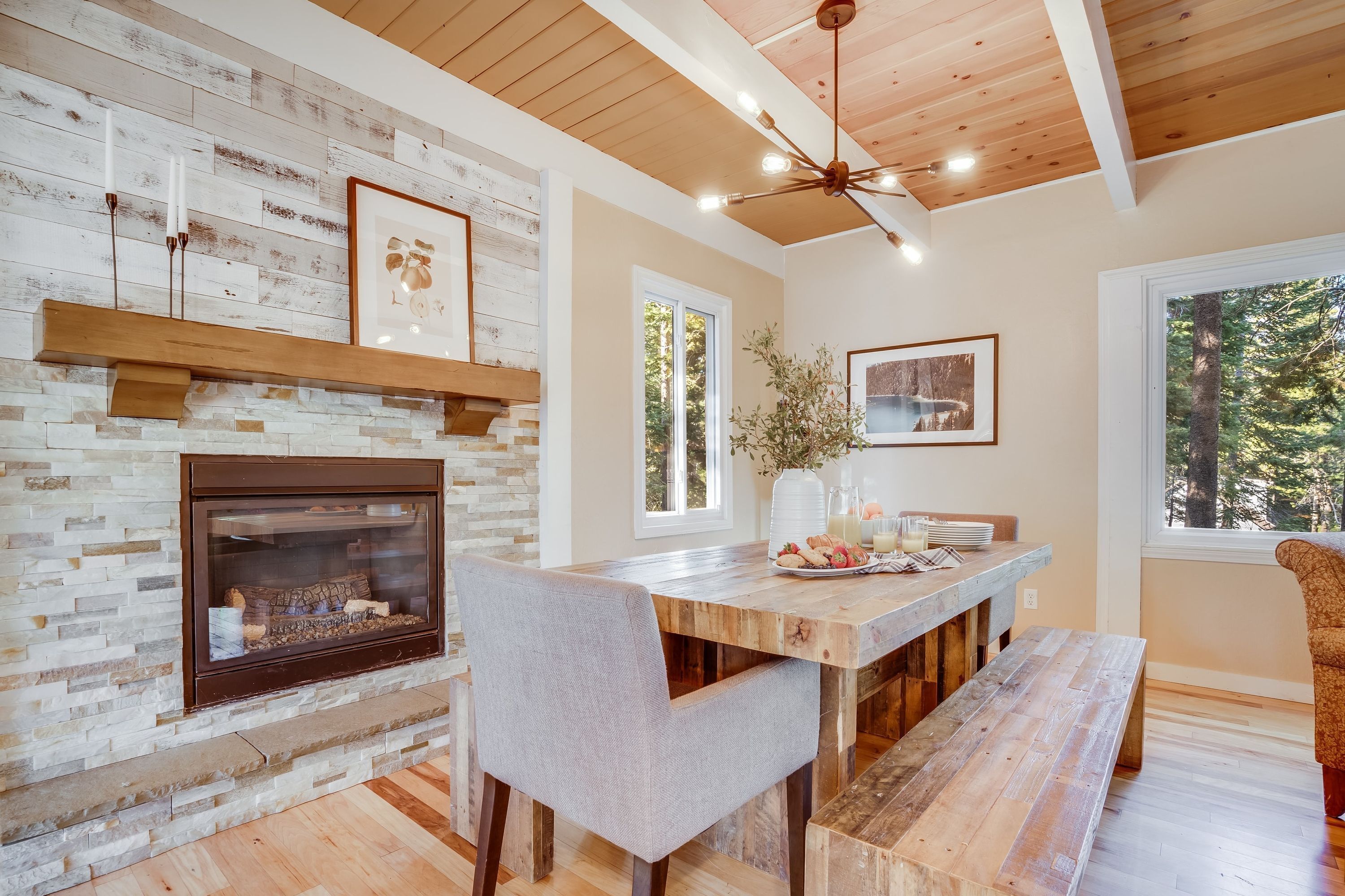 A dining area with a stone fireplace, wooden ceiling, and large windows.