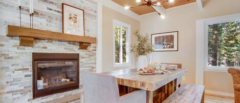 A dining area with a stone fireplace, wooden ceiling, and large windows.