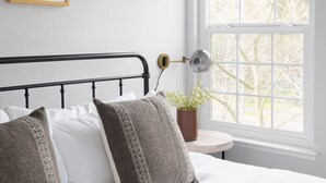 A bedroom with a bed, white walls, a window with a view of trees, a small round table, and a potted plant. - Black Oak by Avantstay Modern Chic Santa Rosa Hideaway With Pool Table Fire Pit (Santa Rosa)