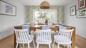 A dining area with a wooden table, white chairs, and a woven pendant light. - Black Oak by Avantstay Modern Chic Santa Rosa Hideaway With Pool Table Fire Pit (Santa Rosa)