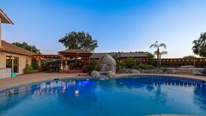 A swimming pool with a rock feature, a covered patio, and a building with outdoor lighting. - Chardonnay Charm by Avantstay Luxe Group Retreat w Pool Mins to Wineries (Temecula)