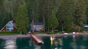 A lakeside cabin with a dock extending into the water, surrounded by dense forest. - Lakefront Haven by Avantstay Minutes to Ski Resorts Private Dock Boat (Homewood)