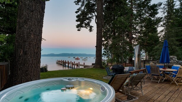 A hot tub on a wooden deck with a view of a lake and dock. - Lakefront Haven by Avantstay Minutes to Ski Resorts Private Dock Boat (Homewood)