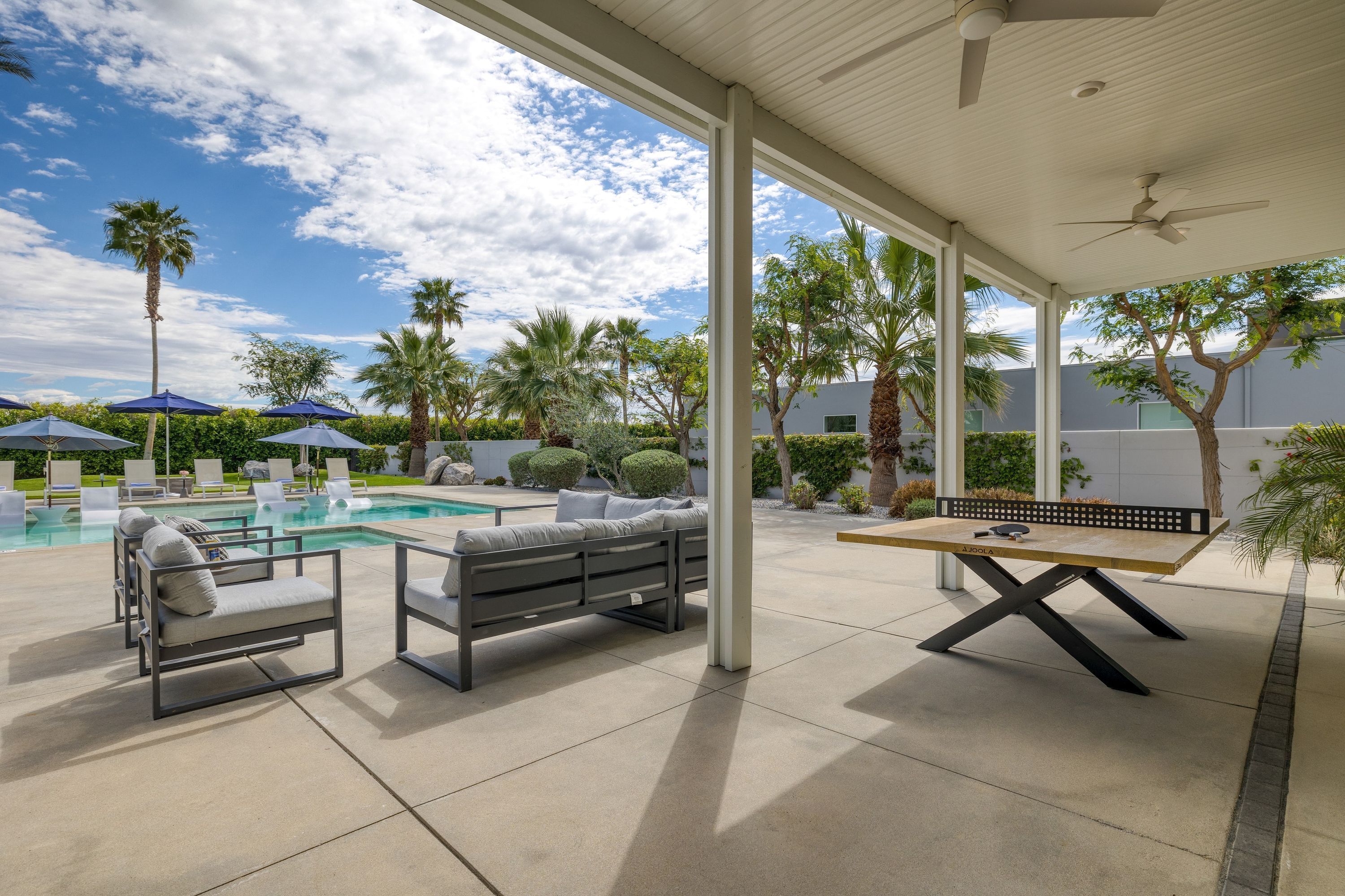A covered outdoor area with a pool, lounge chairs, and a table.
