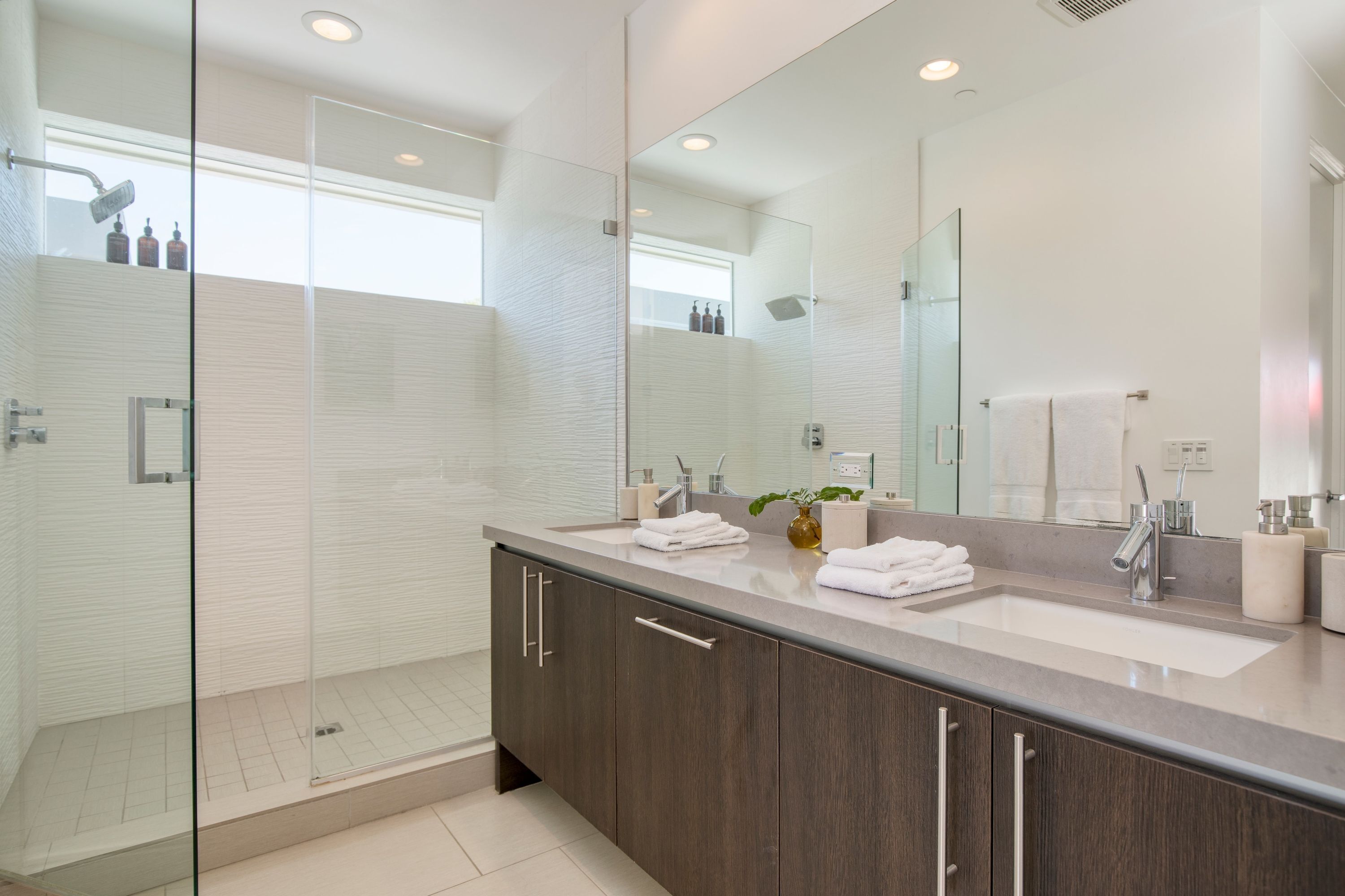 A modern bathroom with a glass-enclosed shower, a large sink with a mirror, and dark wooden cabinets.