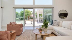 Un salon moderne avec un canapé, une table basse et une grande porte-fenêtre coulissante donnant sur une terrasse extérieure.