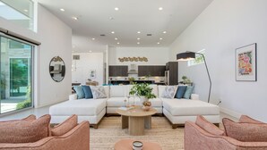Un salon moderne avec un canapé d’angle, une table basse et un coin repas, la cuisine étant visible au fond.