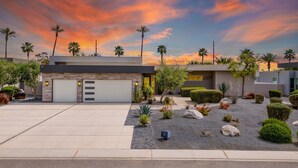 Une maison moderne avec un garage, un jardin aménagé et des palmiers.
