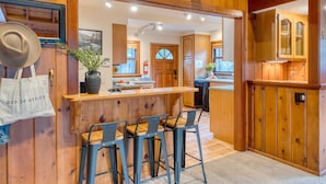 A wooden interior with a bar area, bar stools, and a kitchen visible in the background.