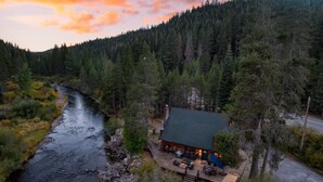 A cabin with a deck overlooking a river, surrounded by dense forest.