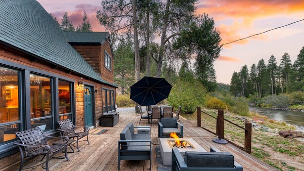 A wooden deck with outdoor seating, a fire pit, and a view of a river and forest.