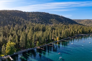 An aerial view of a forested area with a dock extending into a calm lake, surrounded by dense trees. - Homewood Lakefront by Avantstay Private Beach Lake Access Views (Homewood)