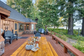 A wooden deck with outdoor seating and a dining table set for a meal. - Homewood Lakefront by Avantstay Private Beach Lake Access Views (Homewood)