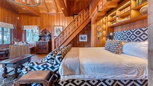 Ein Holzhütten-Interieur mit einem Bett, einer Treppe, einem Esstisch und einem Bücherregal.
