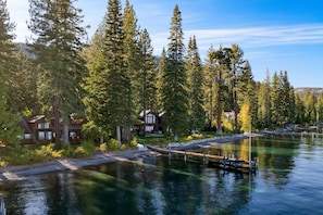 A lakeside property with a dock, surrounded by tall evergreen trees and a house with a deck. - Homewood Lakefront by Avantstay Private Beach Lake Access Views (Homewood)