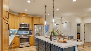 Une cuisine moderne avec des meubles en bois, des appareils en acier inoxydable et un grand îlot central doté d’un plan de travail en marbre.
