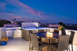 Una terrazza sul tetto con barbecue, vasca idromassaggio e zona pranzo con sedie in vimini.