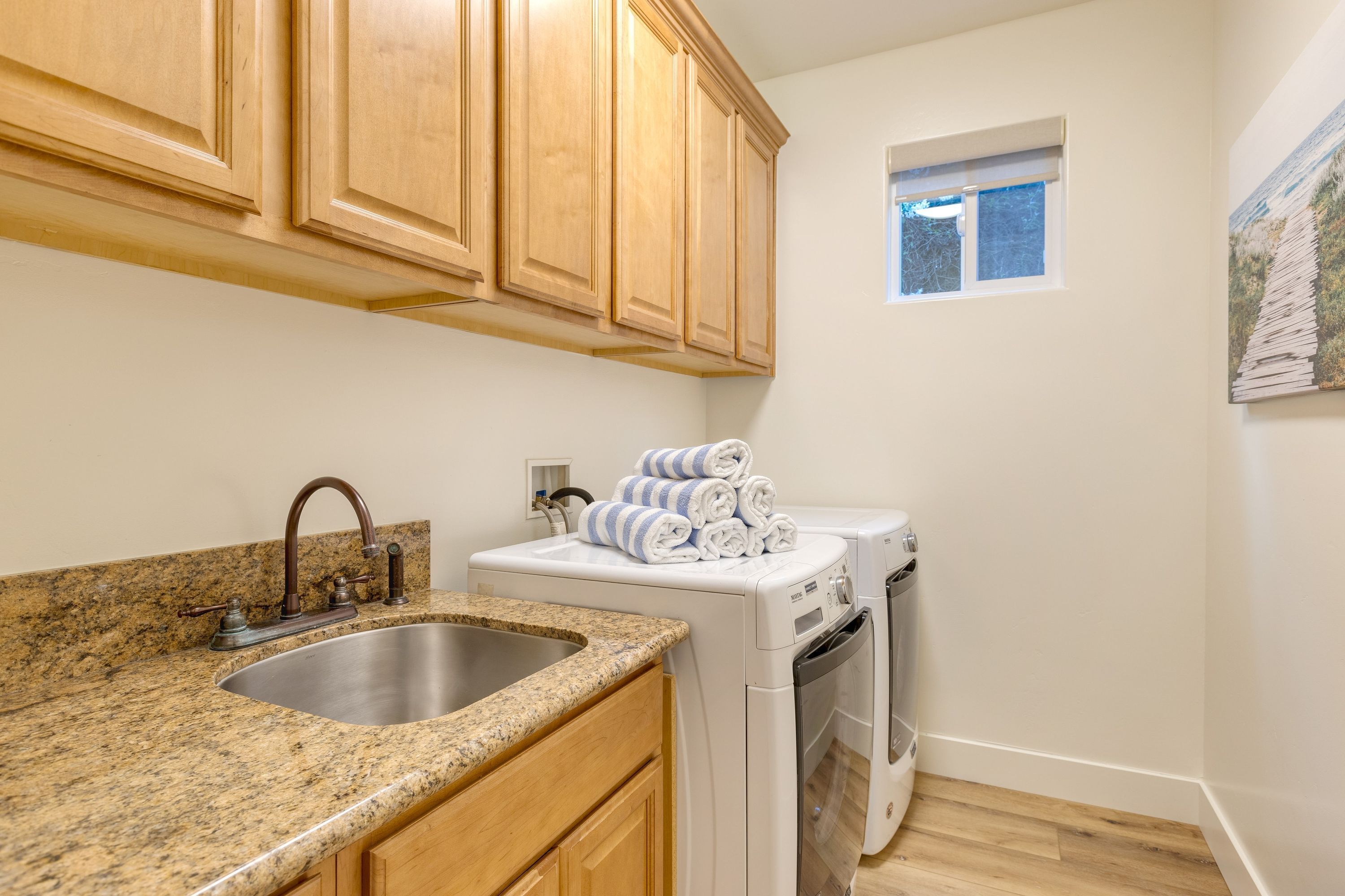 Une cuisine dotée de plans de travail en granit, d’armoires en bois, d’un évier en acier inoxydable, d’un lave-linge et d’un sèche-linge superposés, et d’une petite fenêtre.