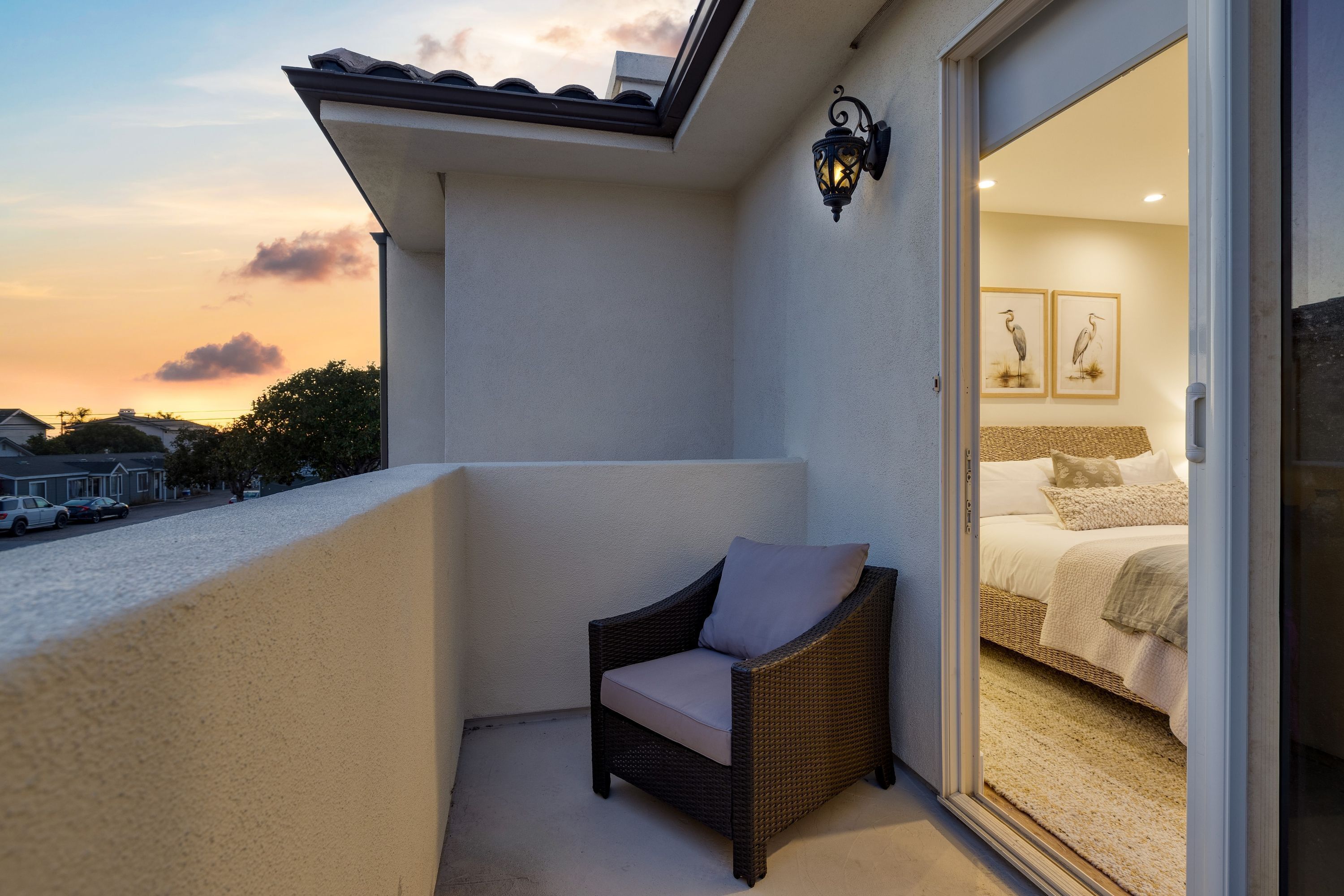 A balcony with a wicker chair and a bed visible through an open door.