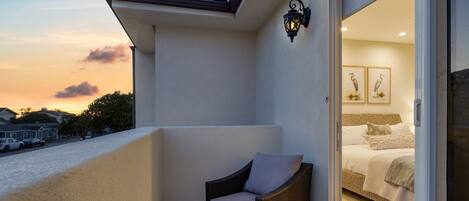 A balcony with a wicker chair and a bed visible through an open door.