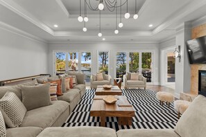 Ein geräumiges Wohnzimmer mit einer großen Couch, zwei Sesseln und einem Couchtisch. Große Fenster bieten Blick auf Bäume und einen Balkon.