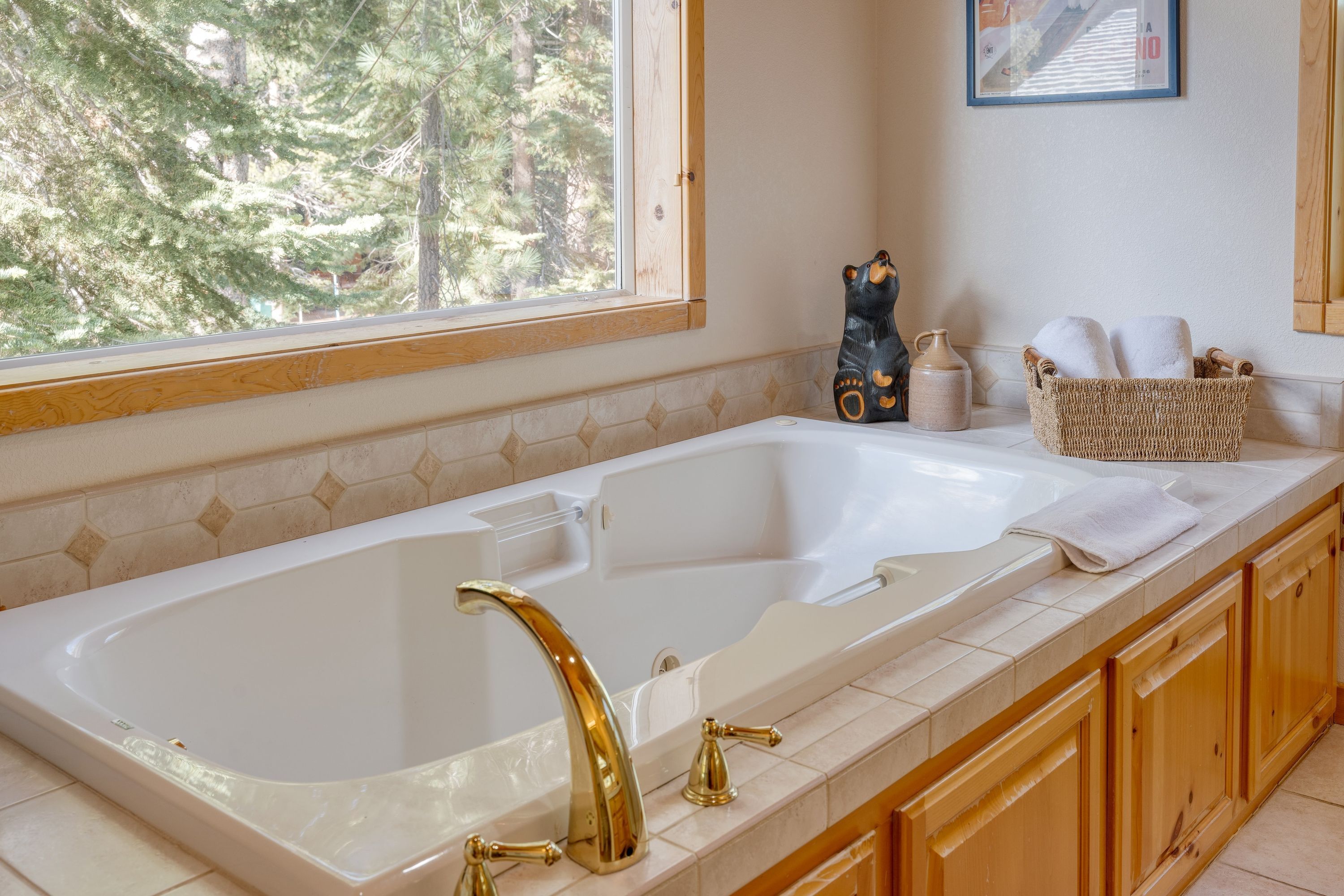 A bathroom with a large bathtub, wooden cabinets, a wicker basket with towels, and a window with a view of trees.
