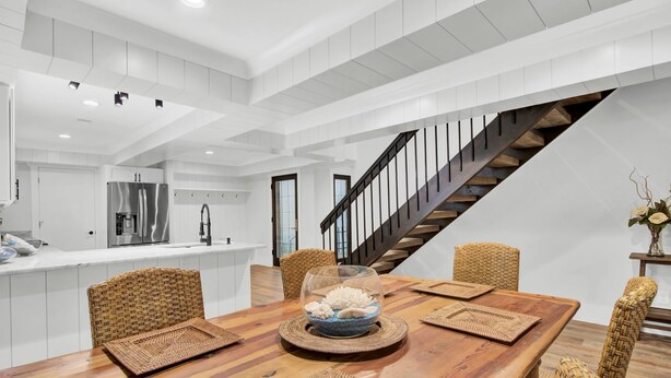 A modern kitchen with white cabinetry, a stainless steel refrigerator, and a wooden dining table with woven placemats and chairs. - Mizzenmast by Avantstay Harbourtown Escape Group Retreat w Patio (Hilton Head Island)