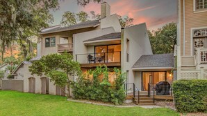 A modern two-story house with a balcony, a covered patio, and a well-maintained lawn. - Mizzenmast by Avantstay Harbourtown Escape Group Retreat w Patio (Hilton Head Island)