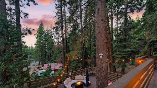 A deck with outdoor seating and string lights, surrounded by tall trees and a forested area. - Washoe Way by Avantstay Luxury Tahoe Retreat A Location w Beach Access (Tahoe City)