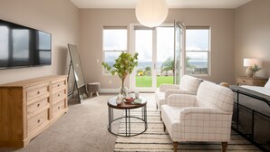 A modern living room with a flat-screen TV, a wooden cabinet, a round coffee table, a white sofa, and a large window with a view of the outdoors.