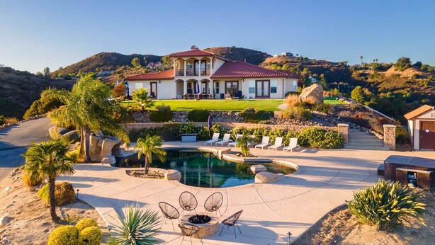 A large house with a pool, surrounded by a landscaped garden and a mountain backdrop.