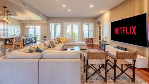 A spacious living room with a large flat-screen TV, comfortable seating, and a view of the outdoors.