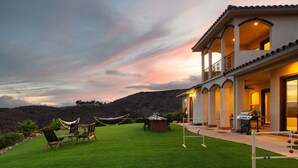 A two-story house with a balcony, a dining area with outdoor furniture, and a well-maintained lawn.