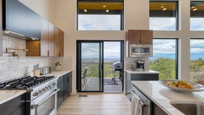 Une cuisine moderne dotée d’une grande cuisinière, d’un four et offrant une vue sur l’extérieur grâce à une porte-fenêtre coulissante.