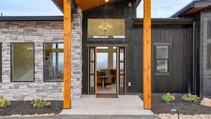 Une maison moderne avec une façade en pierre, de grandes fenêtres et un porche en bois.