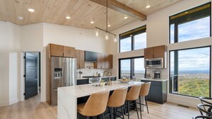 Une cuisine moderne dotée d’un îlot central, d’appareils électroménagers en acier inoxydable et de grandes fenêtres offrant une vue sur le paysage.
