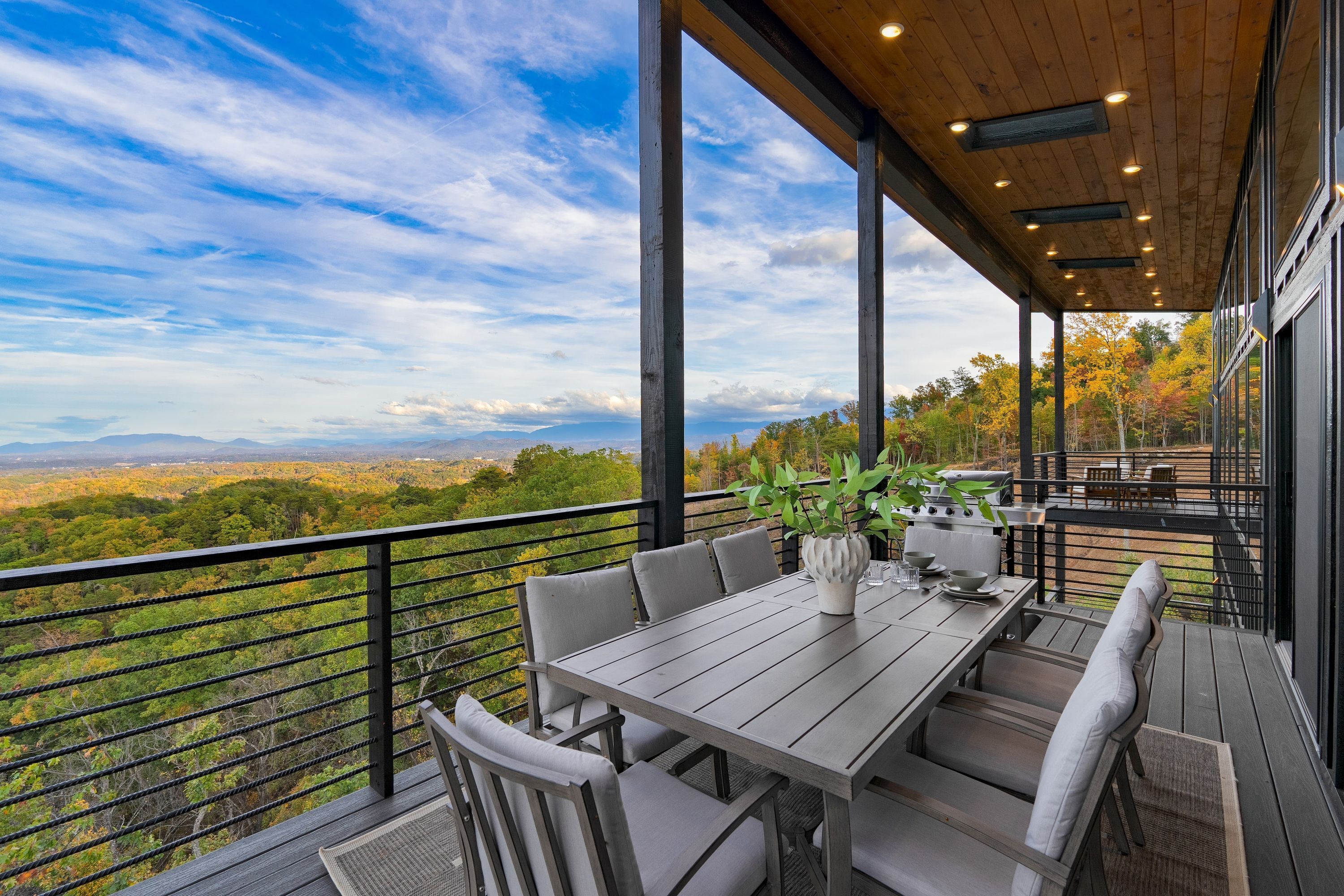 A covered outdoor dining area with a table and chairs, a potted plant, and a grill.