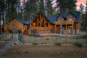 A log cabin with a balcony, a staircase leading to the main entrance, and a fenced yard.