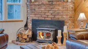 Un salon chaleureux avec une cheminée en briques, des canapés en cuir, une table basse en bois ornée de pommes de pin et une horloge au mur.