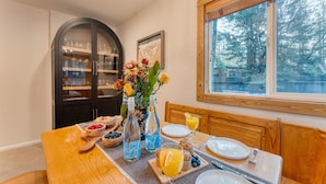 Une table de petit-déjeuner dressée avec une variété de plats et de boissons, un vase rempli de fleurs et une vue sur les arbres par la fenêtre.