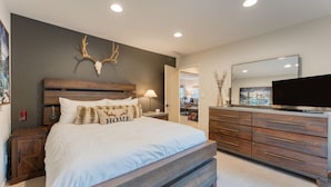 Une chambre à coucher avec un grand lit, une tête de lit en bois, un crâne de cerf accroché au mur et une commode avec un miroir.