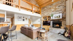 A spacious living area with a stone fireplace, a wooden ceiling, and a loft with a wooden railing. - Jackhorn By Avantstay Spectacular Cozy Cabin w Hot Tub (Big Bear Lake)
