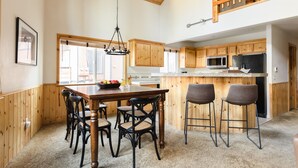 A spacious kitchen with wooden cabinets, a large island with bar stools, and a hanging light fixture. - Jackhorn By Avantstay Spectacular Cozy Cabin w Hot Tub (Big Bear Lake)