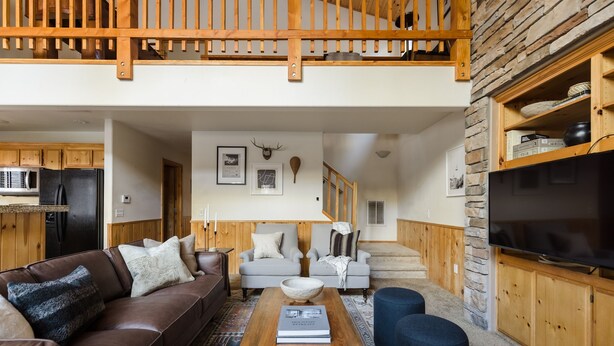 A spacious living room with a brown leather sofa, a wooden coffee table, and a grey sofa. A staircase with wooden railings leads to an upper level. - Jackhorn By Avantstay Spectacular Cozy Cabin w Hot Tub (Big Bear Lake)