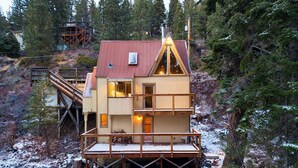 Une cabane dotée d’une terrasse en bois, d’un escalier en métal et d’un toit rouge.