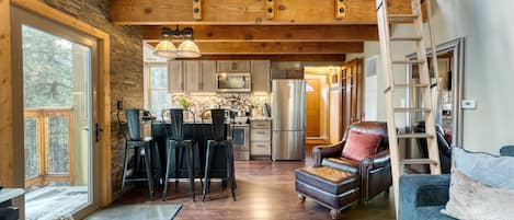 A spacious living area with a high ceiling, wooden beams, a dining area with chairs, a sofa, and a ladder.