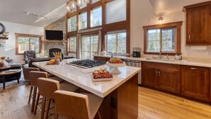 A spacious kitchen with a large island, wooden cabinets, and a stone fireplace. - Denton by Avantstay Hot Tub Enclosed Deck w Fire Pit Near Skiing Lake (Truckee)