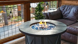 A round outdoor fire pit with a metal railing, surrounded by a wooden deck and a brown leather sofa. - Denton by Avantstay Hot Tub Enclosed Deck w Fire Pit Near Skiing Lake (Truckee)