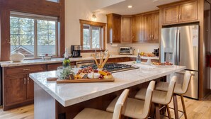 A spacious kitchen with wooden cabinets, a large island with bar stools, stainless steel appliances, and a window providing natural light. - Denton by Avantstay Hot Tub Enclosed Deck w Fire Pit Near Skiing Lake (Truckee)